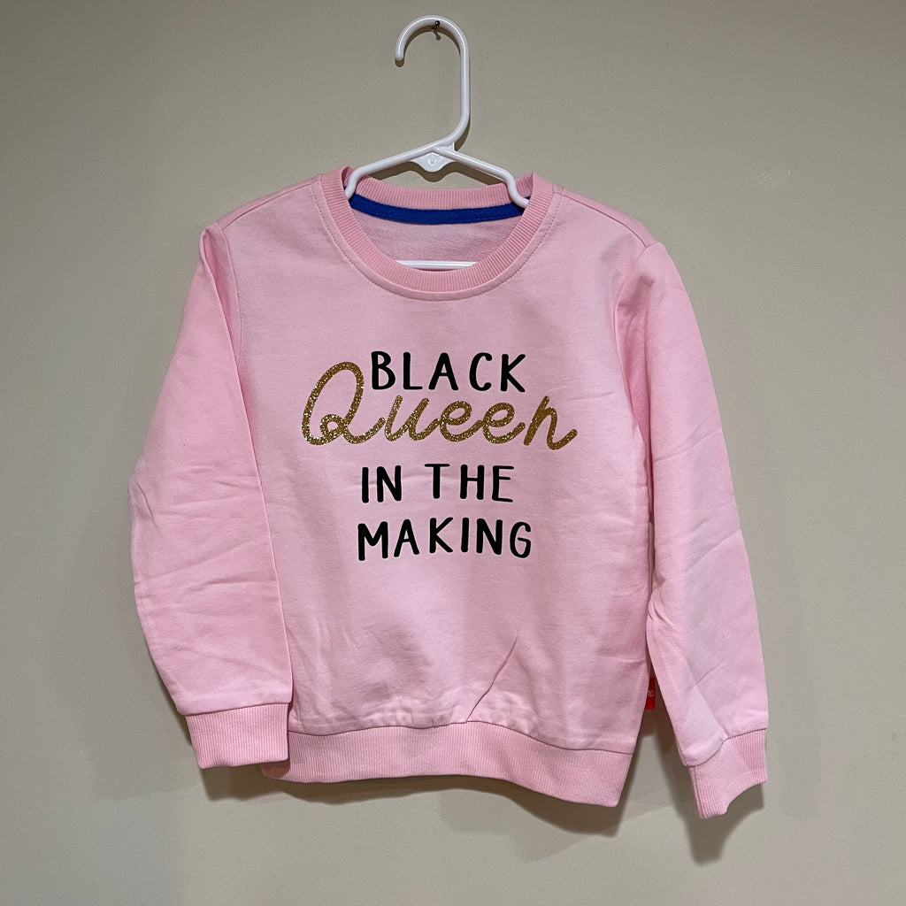 pink sweater with black in the making printed in black and Queen printed in gold glittler