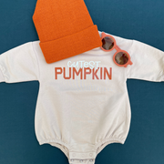 The “Cutest Pumpkin” bubble romper styled with an orange knit beanie and matching sunglasses, creating the perfect cozy fall look.