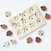 The ladybug puzzle with its pieces removed, revealing numbered slots for easy learning, surrounded by scattered ladybug pieces in natural wood tones.