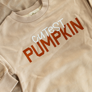 A close-up of the “Cutest Pumpkin” text on the romper, showing the playful mix of white and burnt orange letters on the soft, organic fabric.