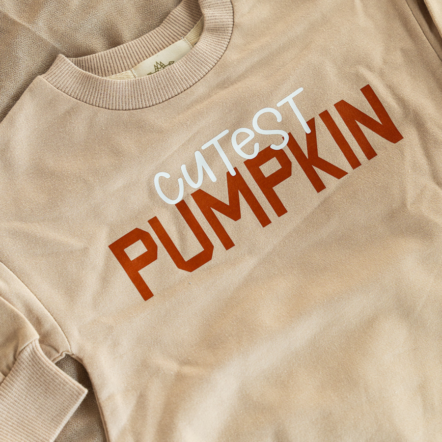 A close-up of the “Cutest Pumpkin” text on the romper, showing the playful mix of white and burnt orange letters on the soft, organic fabric.